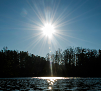 Sunlight reflecting across a lake beneath a tree-lined shore.